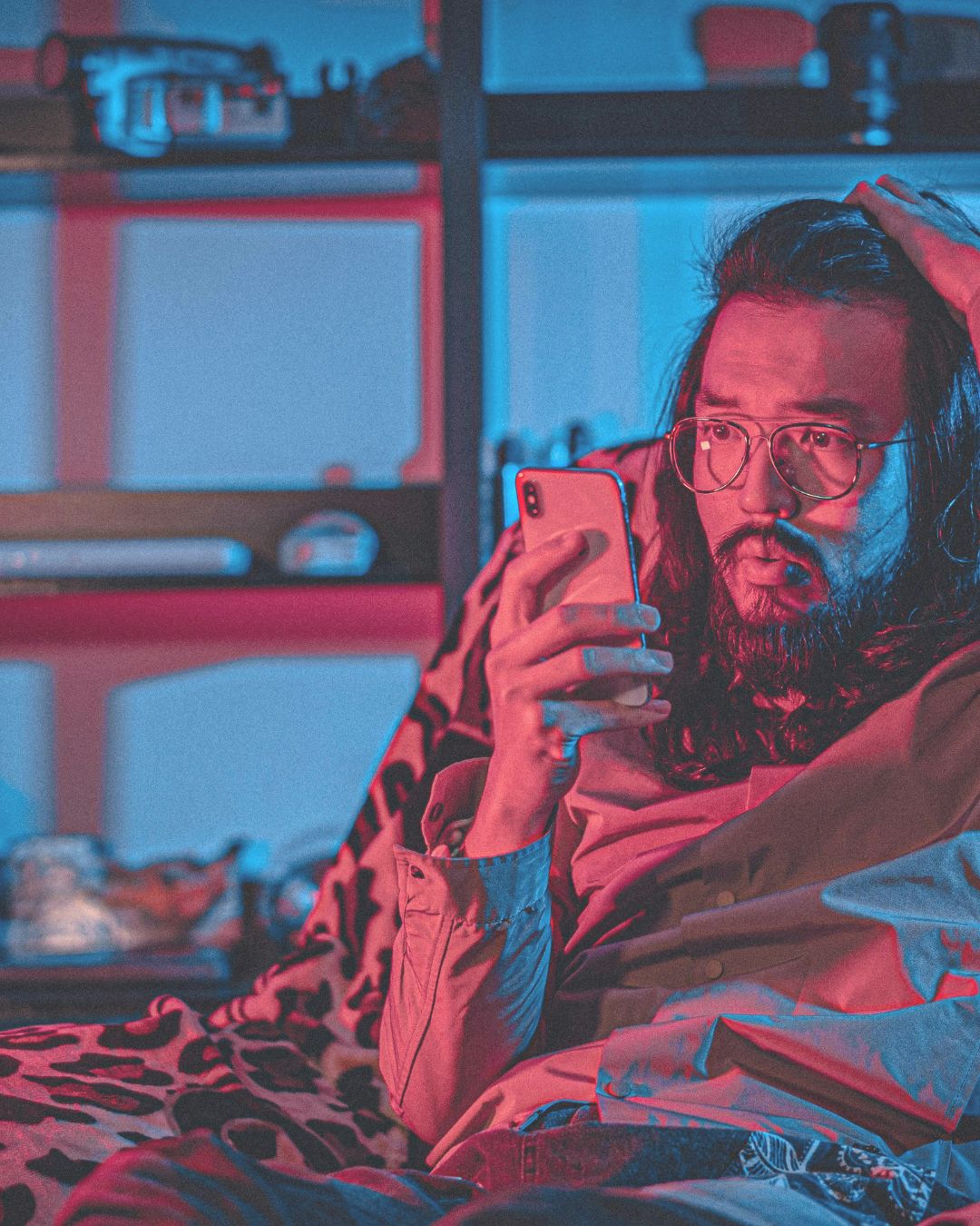 Fake News Website Ein langhaariger Mann mit Brille und Bart schaut besorgt auf sein Smartphone, Hand am Kopf.