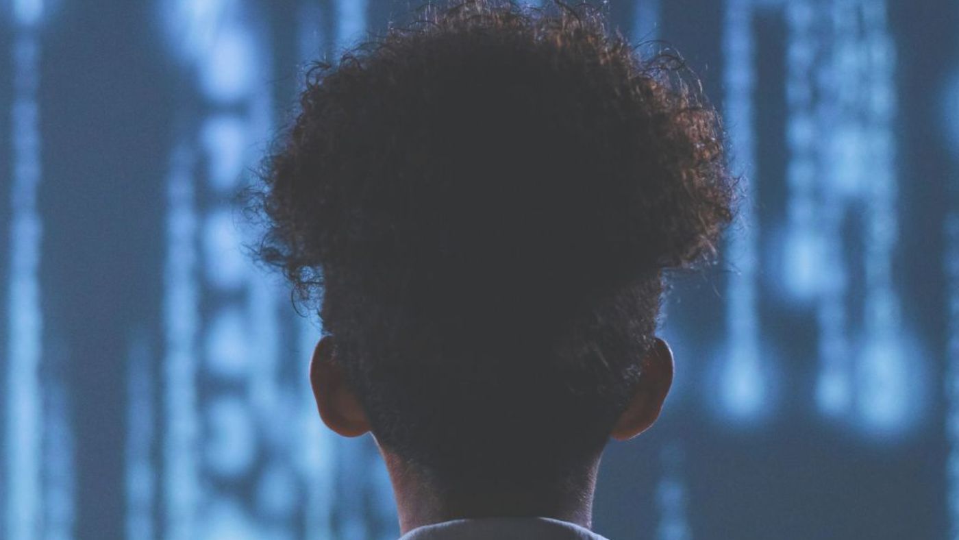 Eine Person mit lockigem Haar von hinten vor einer digitalen Matrix aus blauen Zahlen und Symbolen.
