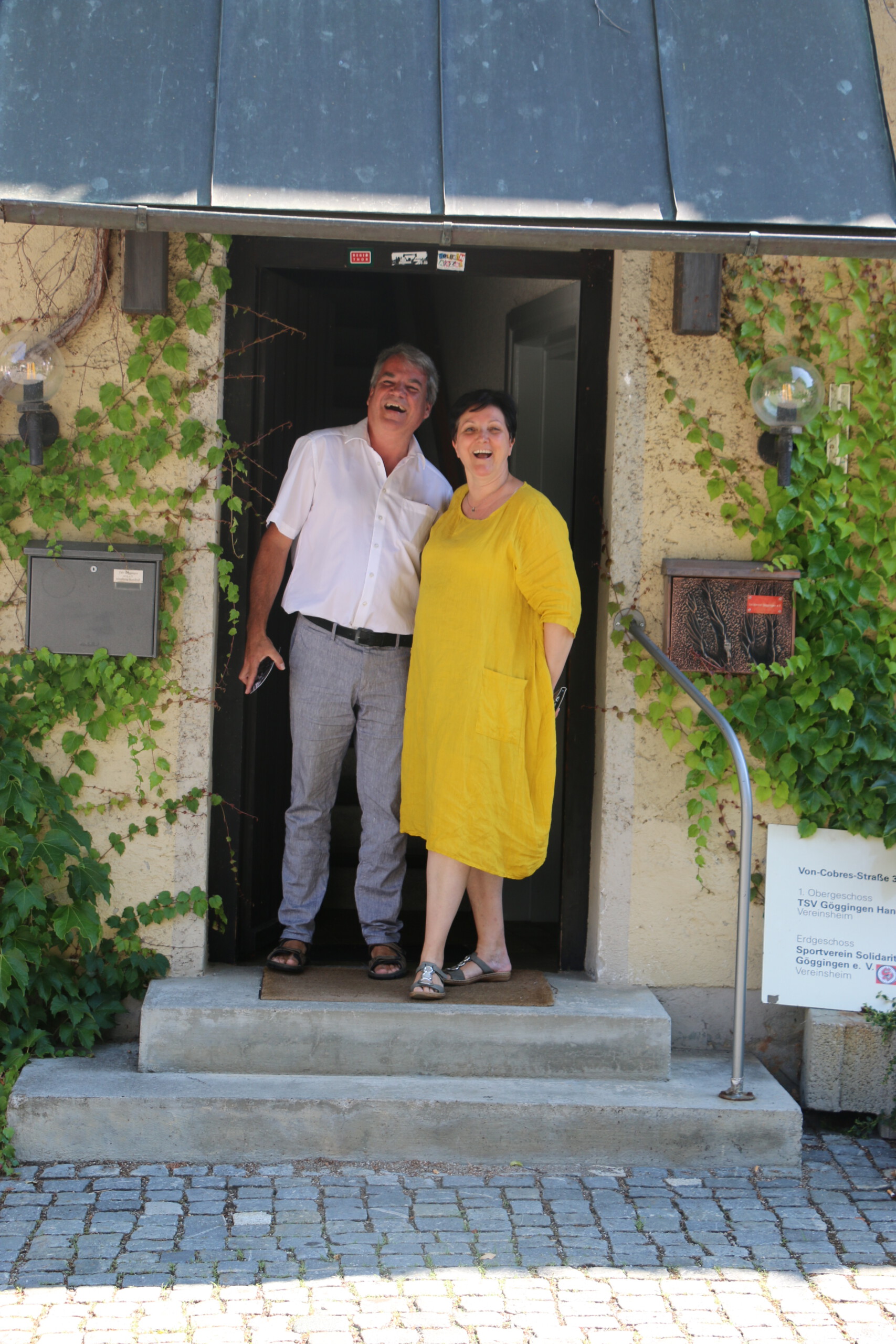 Ein Mann und eine Frau stehen nebeneinander Arm in Arm in einem Hauseingang und lachen