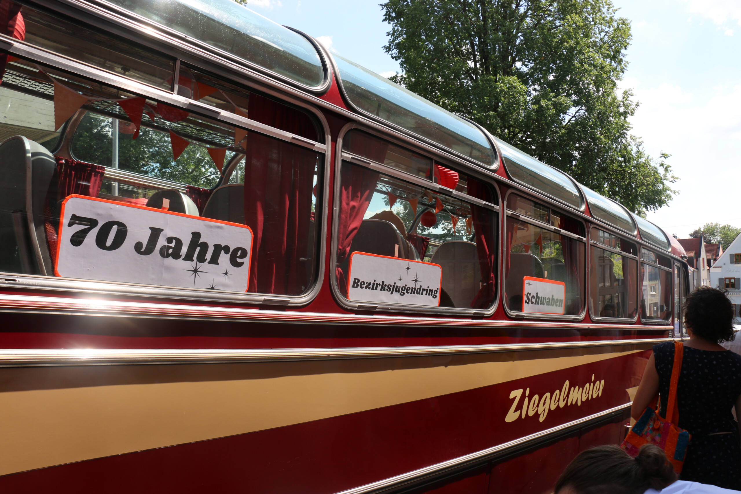 An den Fenstern eines rot-beigen Oldtimer-Buses kleben drei Schilder: 70 Jahre, Bezirksjugendring, Schwaben