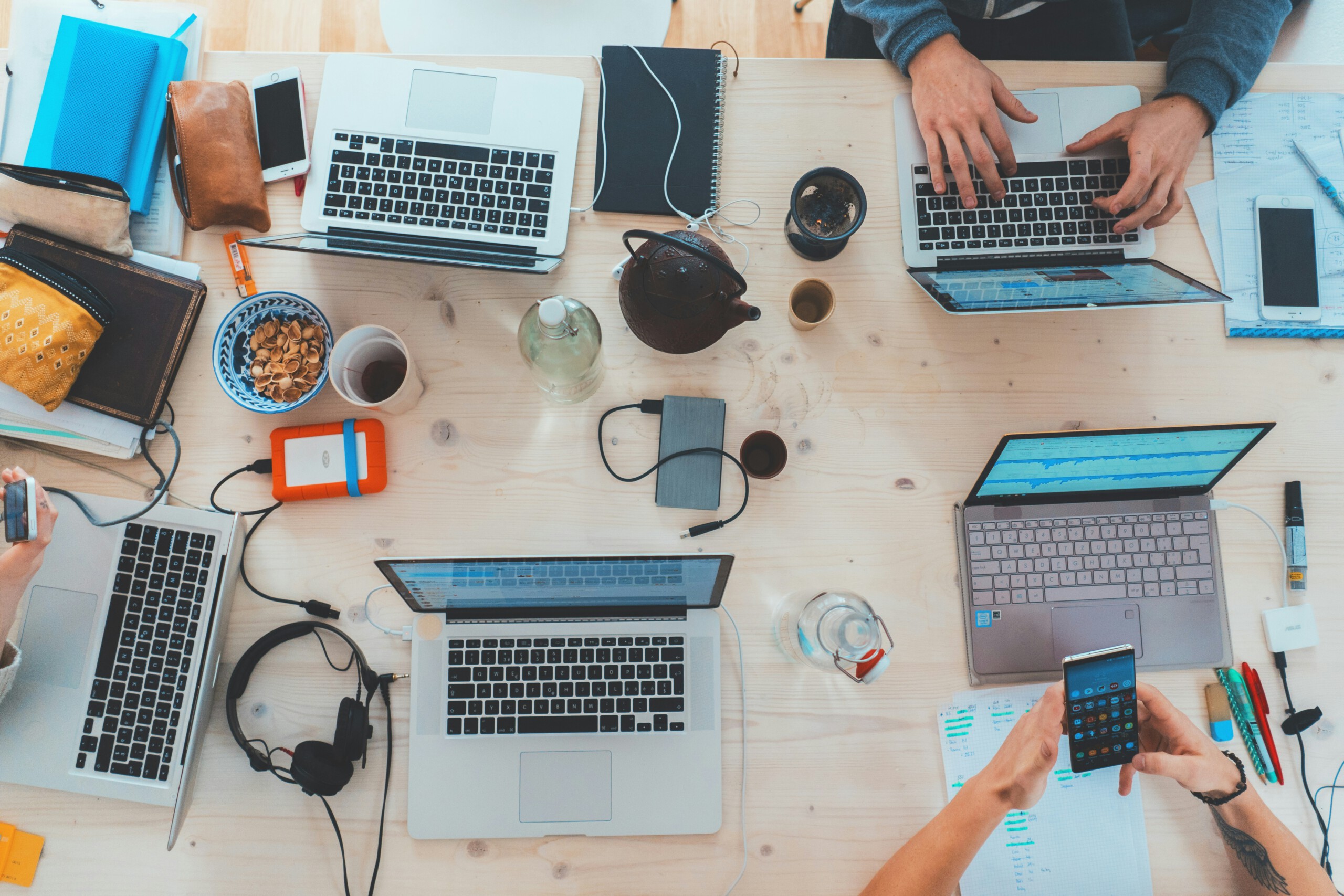 Blick von oben auf einen Holztisch voller Laptops, Getränken und digitalem Zubehör